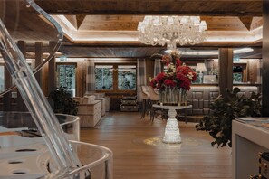 A spacious lobby with a chandelier, wooden flooring, and a large vase of flowers. - Ultima Hotel Gstaad (Saanen)