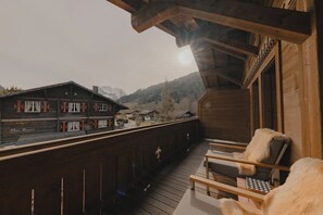 A wooden deck with a view of a mountain village. - Ultima Hotel Gstaad (Saanen)