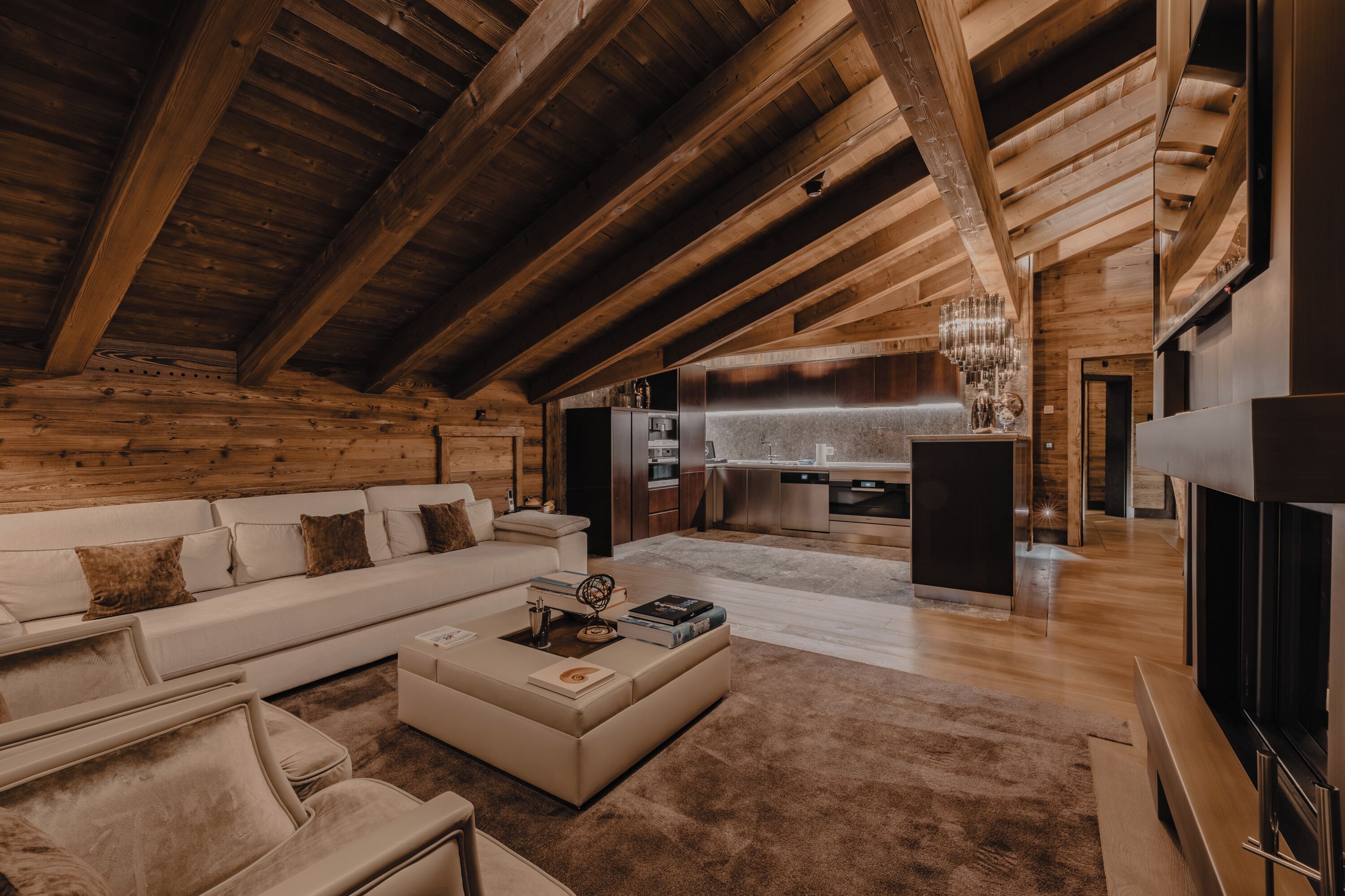 Amplia sala de estar con techo alto, vigas de madera, cocina moderna y un rincón de descanso acogedor.