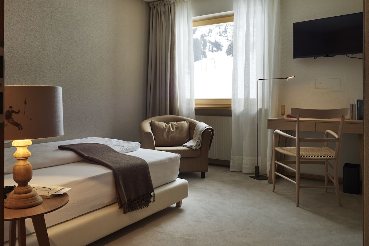 A hotel room with a bed, a desk, a chair, a television, and a window with curtains.