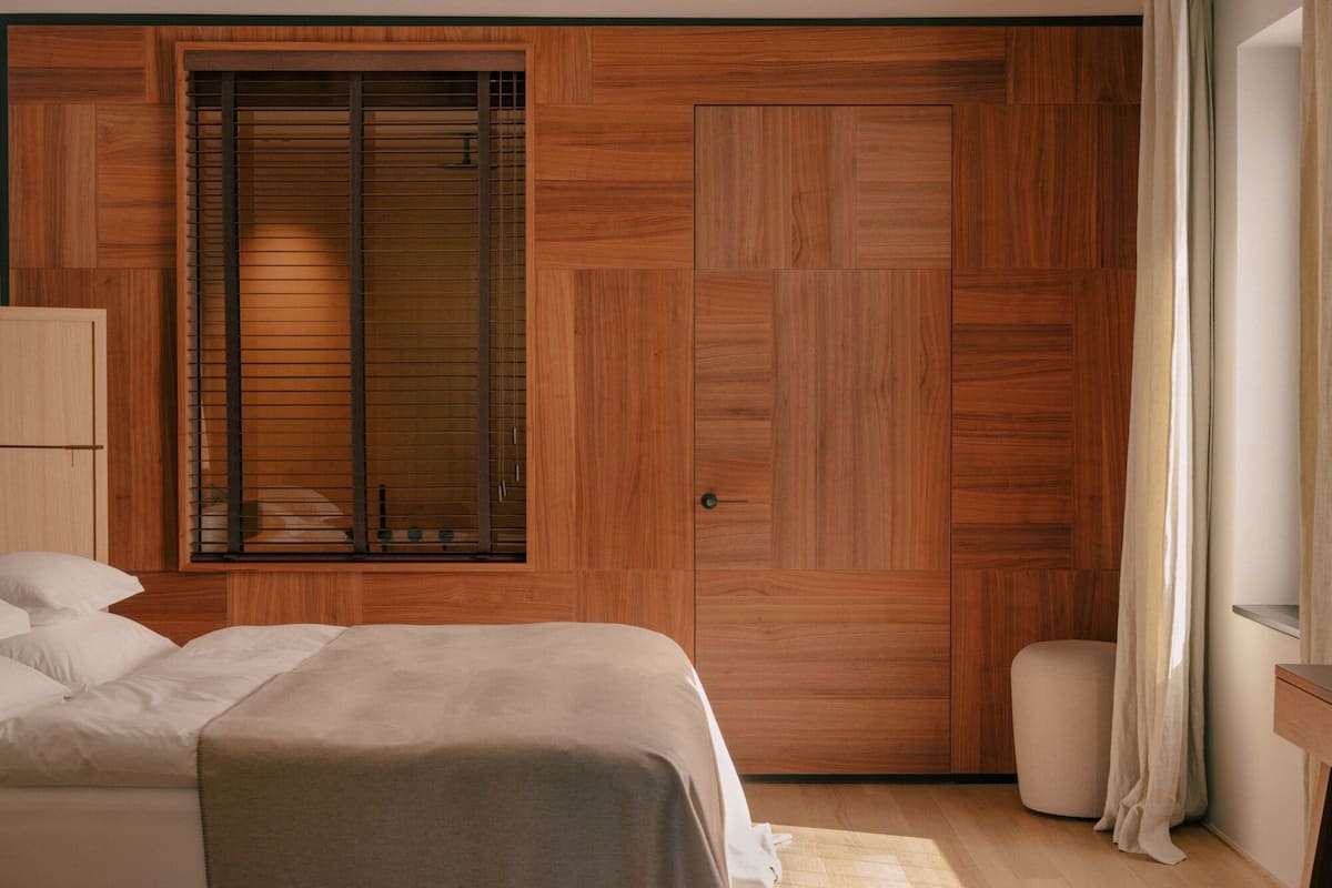 A bedroom with a bed, a wardrobe, a window with blinds, and a bedside table.