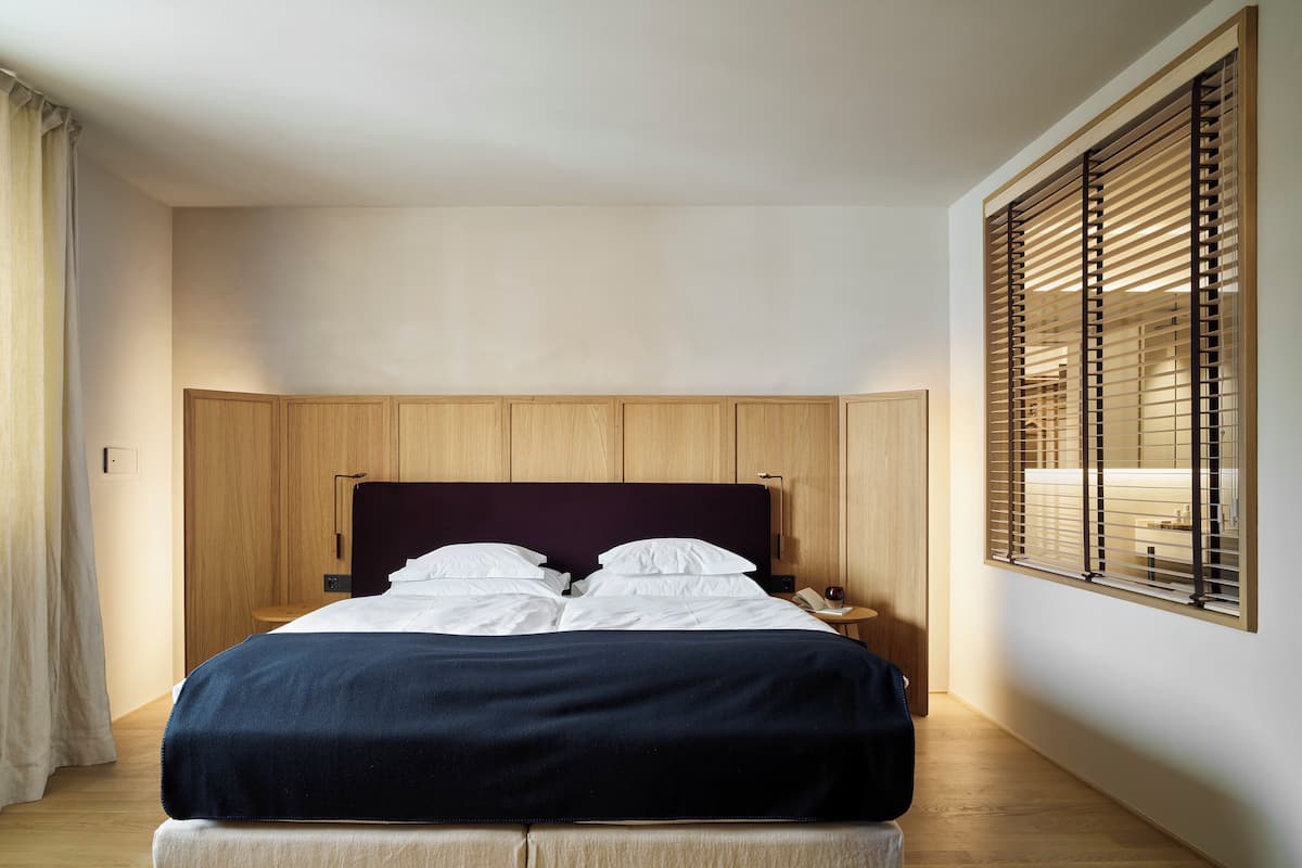 A neatly made bed with white linens and a dark blue blanket, wooden headboard, and a small bedside table with a lamp.