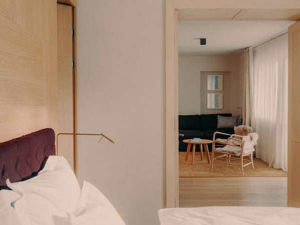 Una habitación de hotel con una cama, una puerta de madera y vistas a una sala de estar con un sofá, sillas y un osito de peluche.