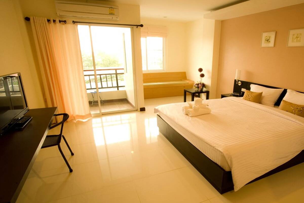 Une chambre d’hôtel comprenant un lit, un bureau avec un ordinateur, une chaise, une table de chevet et une fenêtre avec des rideaux.