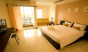 A hotel room with a bed, a desk with a computer, a chair, a nightstand, and a window with curtains.