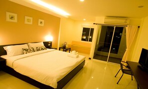 A hotel room with a large bed, a desk, a chair, a TV, and a balcony with a glass door.