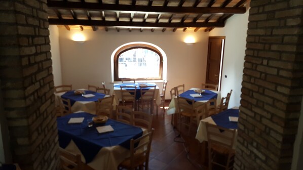 A dining area with tables covered in blue tablecloths, wooden chairs, and a brick wall. - Il Merangolo (Montebuono)