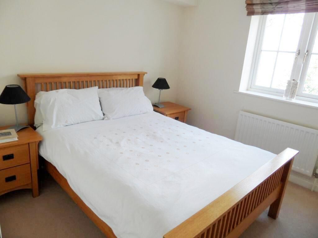 A bedroom with a wooden bed, two bedside tables with lamps, a window with a view, and a radiator.