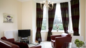 A living room with a red sofa, a glass coffee table, a TV, and a window with curtains. - Sherborne House (Basingstoke)