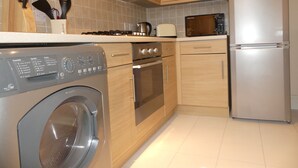 A modern kitchen with stainless steel appliances, wooden cabinets, and a built-in washing machine. - Sherborne House (Basingstoke)