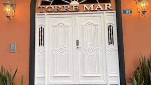 A hotel entrance with a double door, the name "TORRE MAR" above, and a number "104" on the wall.