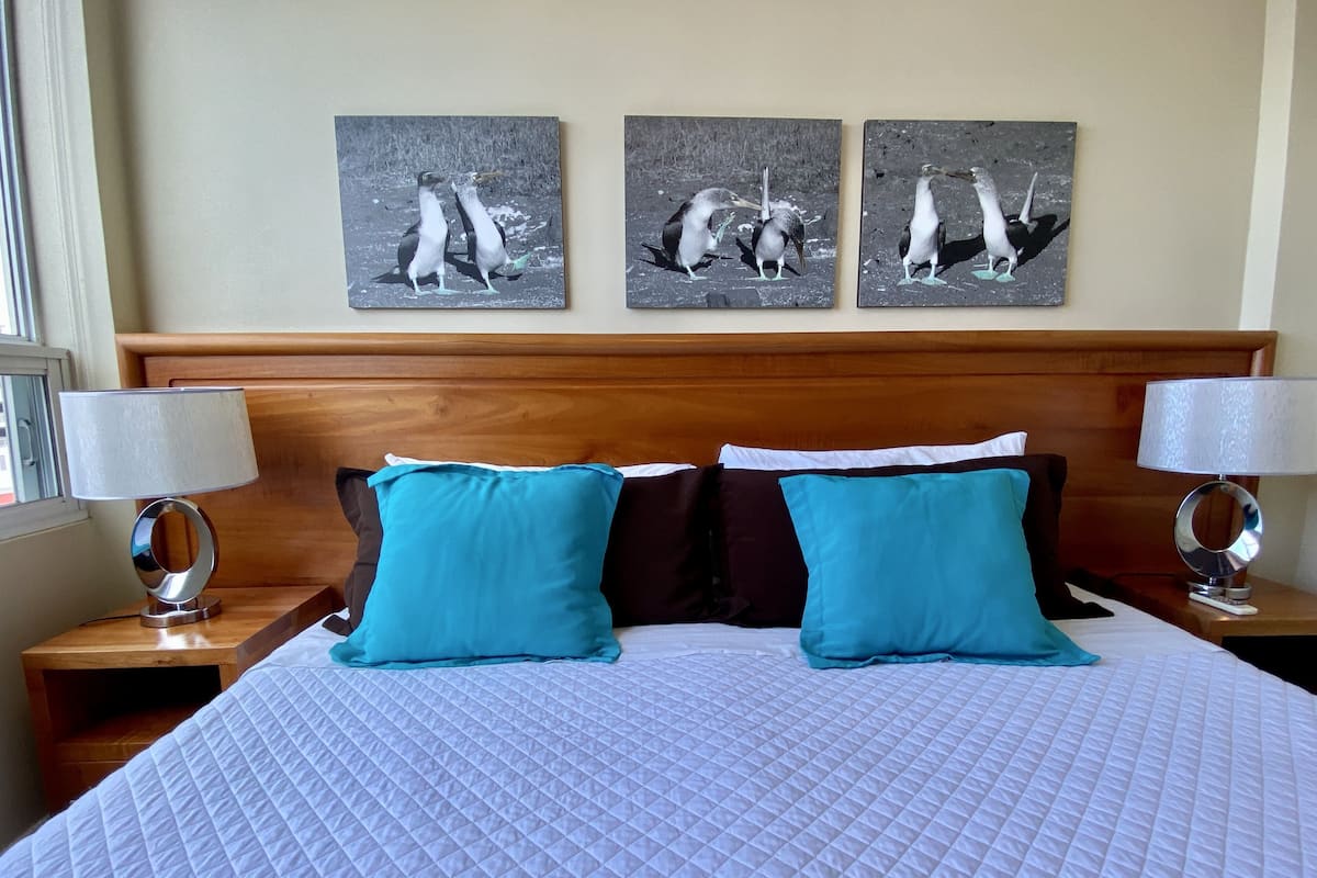 A hotel room with a large bed, two side tables with lamps, and three wall-mounted paintings of birds.