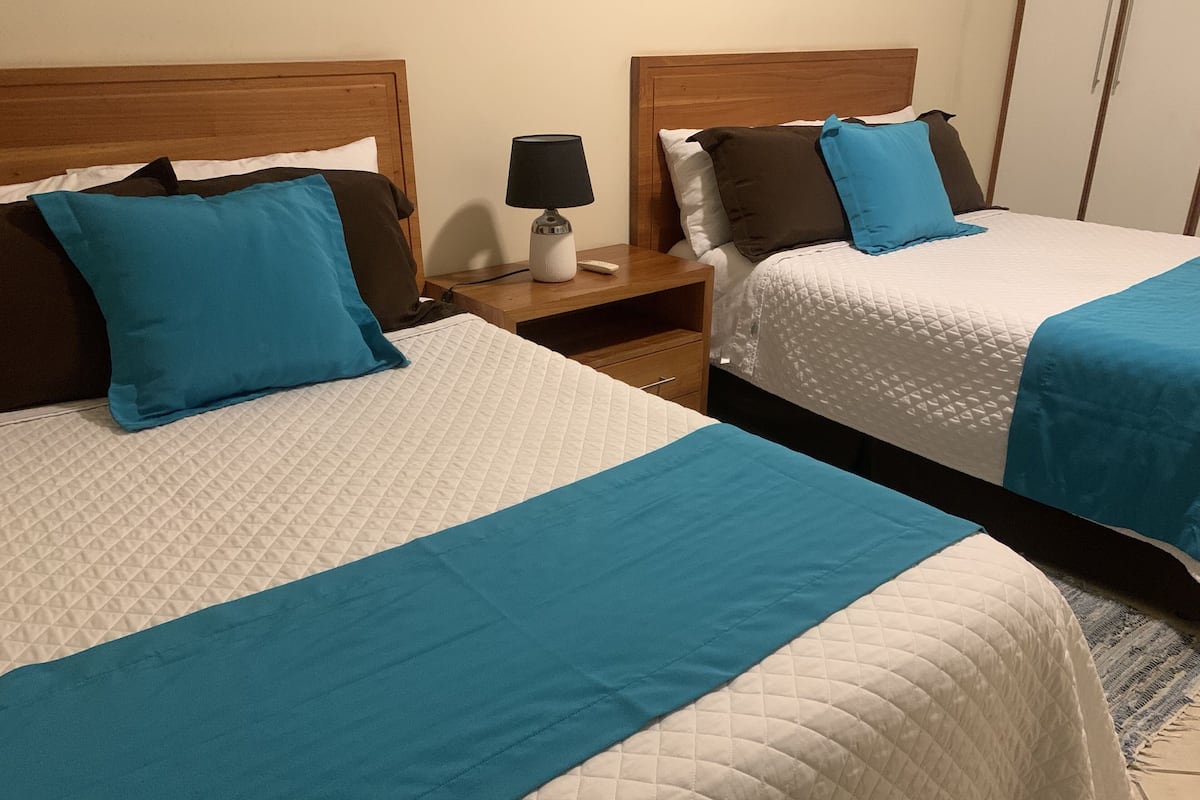 Two beds with blue and white bedding, a nightstand with a lamp, and a wooden headboard.