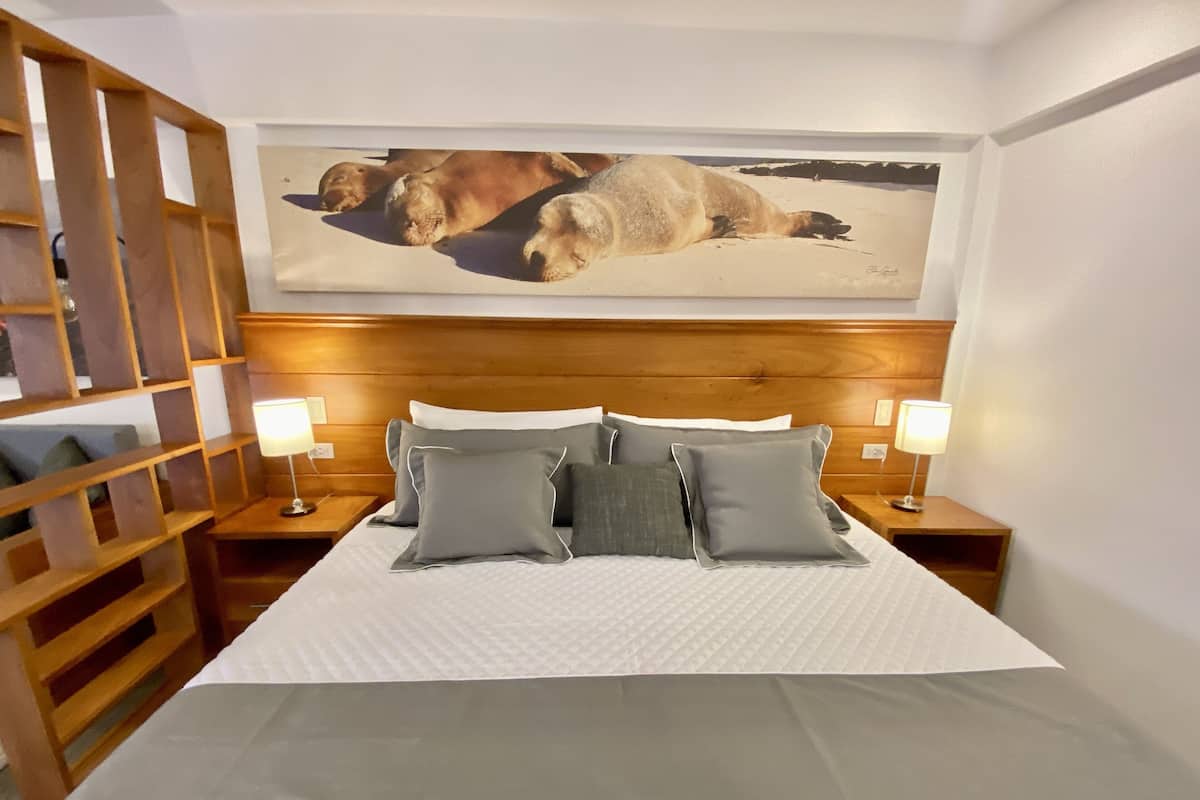 A hotel room with a large bed, two bedside tables with lamps, a wooden headboard, and a painting of seals on the wall.