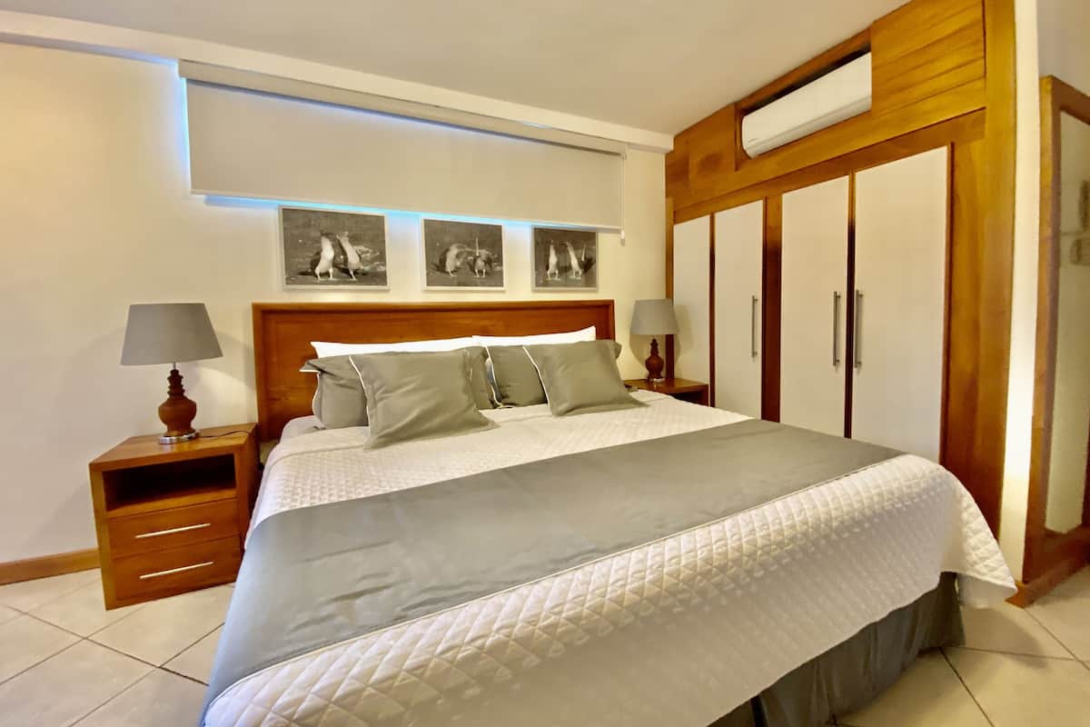 A neatly made bed with a grey and white duvet, wooden headboard, and bedside tables with lamps. There are three framed pictures on the wall above the bed.