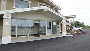 Un edificio con vestíbulo cubierto, amplias ventanas y un estacionamiento con un automóvil.