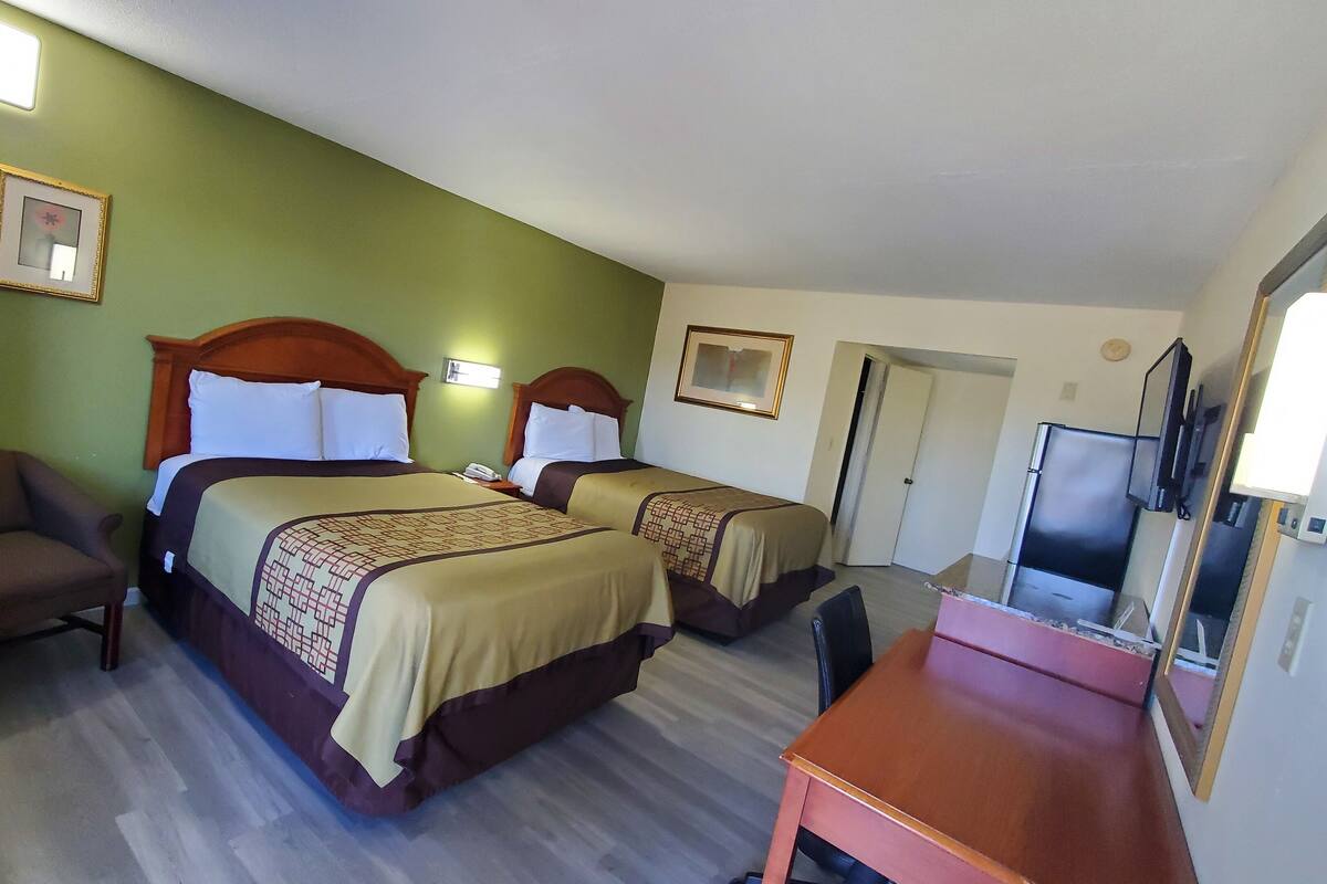 A hotel room with two beds, a chair, a desk, and a TV.
