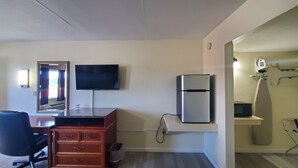 Habitación de hotel con televisor de pantalla plana, refrigerador, cómoda de madera y espejo.