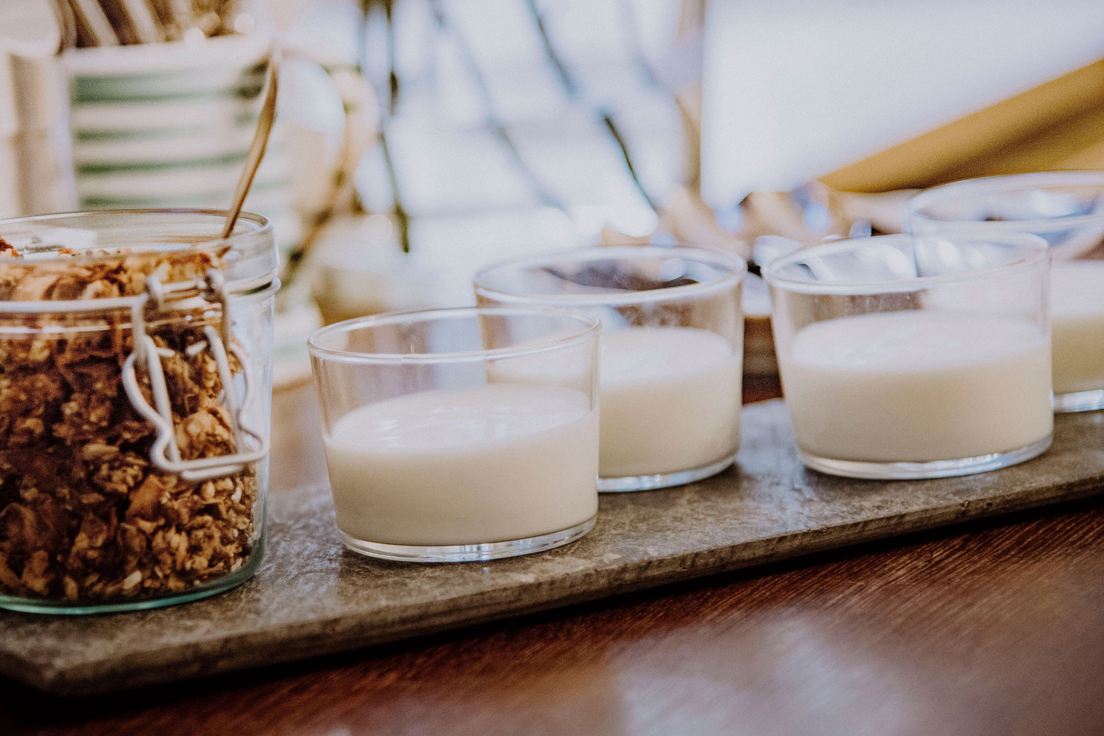 Ein Tablett mit drei Gläsern Milch und einem Kleinglas Granola.