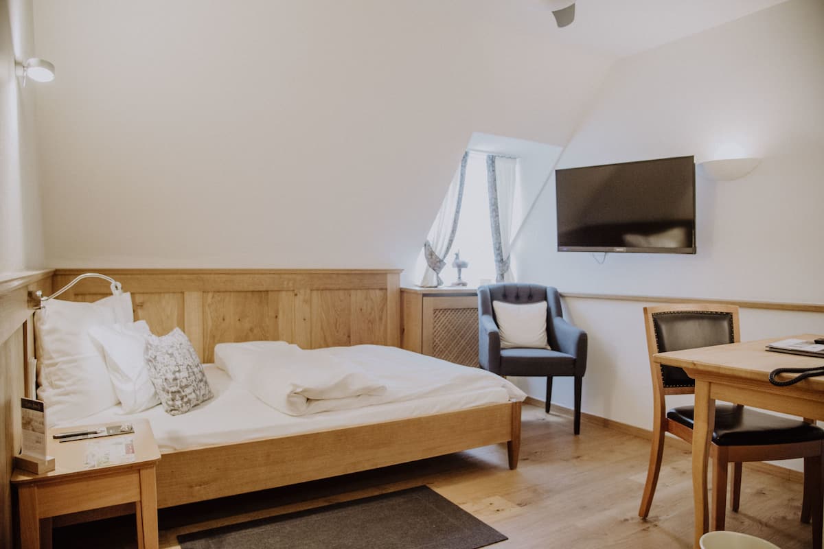 A bedroom with a wooden bed, a desk, a chair, a television, and a window with curtains.