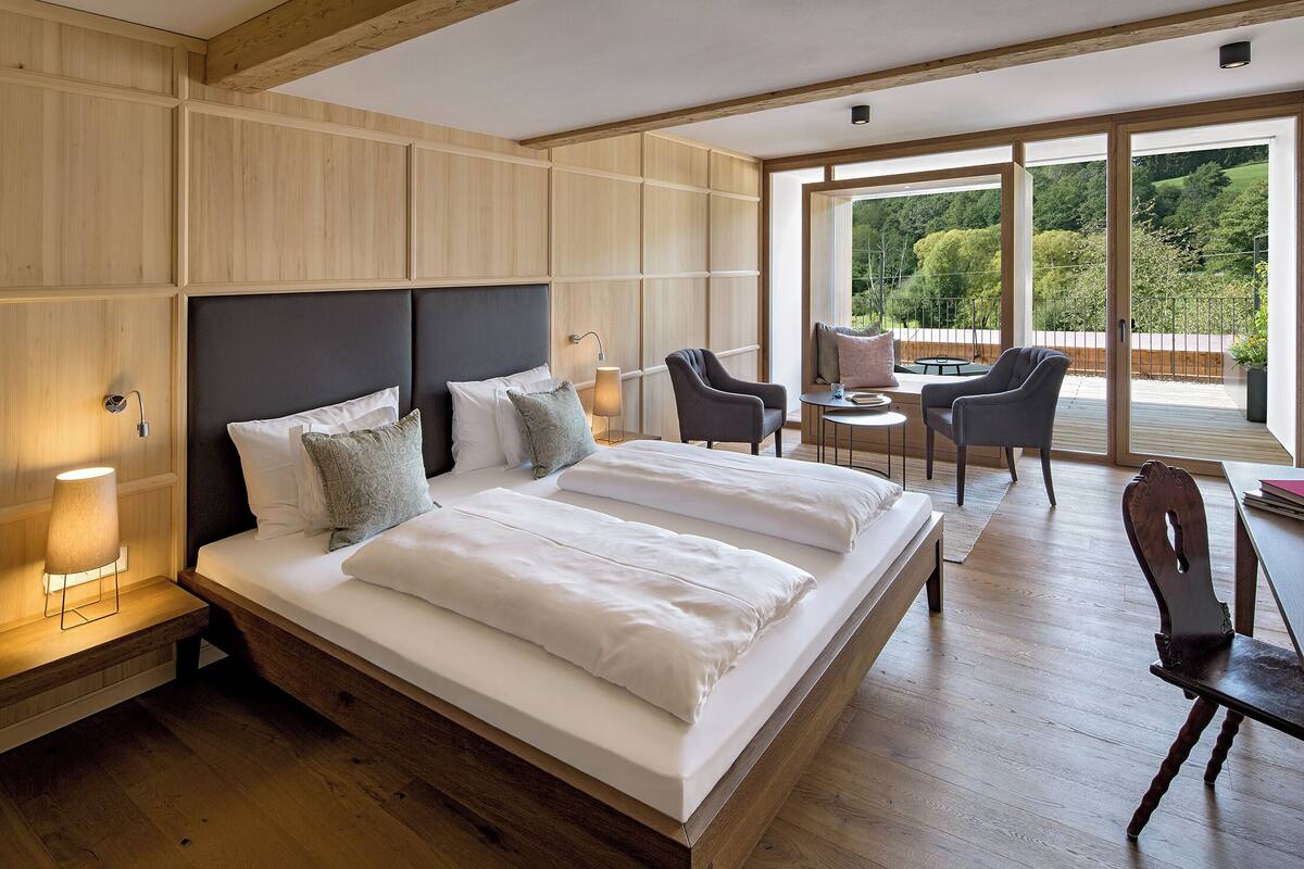 A modern bedroom with a large bed, bedside lamps, and a view of the outdoors.