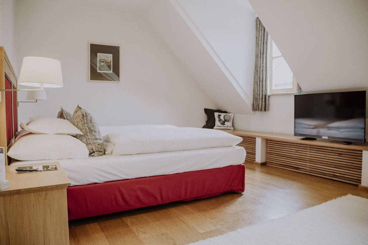 A bedroom with a bed, a TV, a bedside table, and a window.