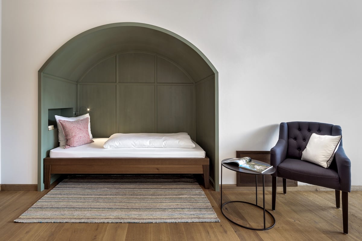 A bedroom with a bed, a chair, a small table, and a rug.