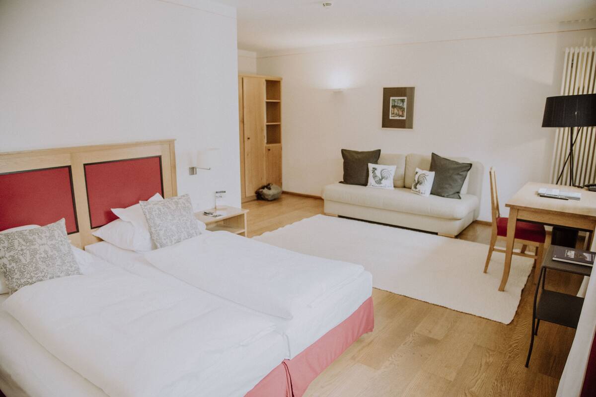 A hotel room with two beds, a sofa, a desk, and a lamp.