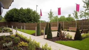 Un espace paysager aménagé en jardin, avec une clôture en bois, des bancs et un chemin pavé.