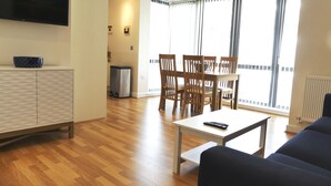 Un salon équipé d’un téléviseur à écran plat, d’une table à manger avec des chaises, d’un canapé et d’une petite table sur laquelle se trouve une télécommande.