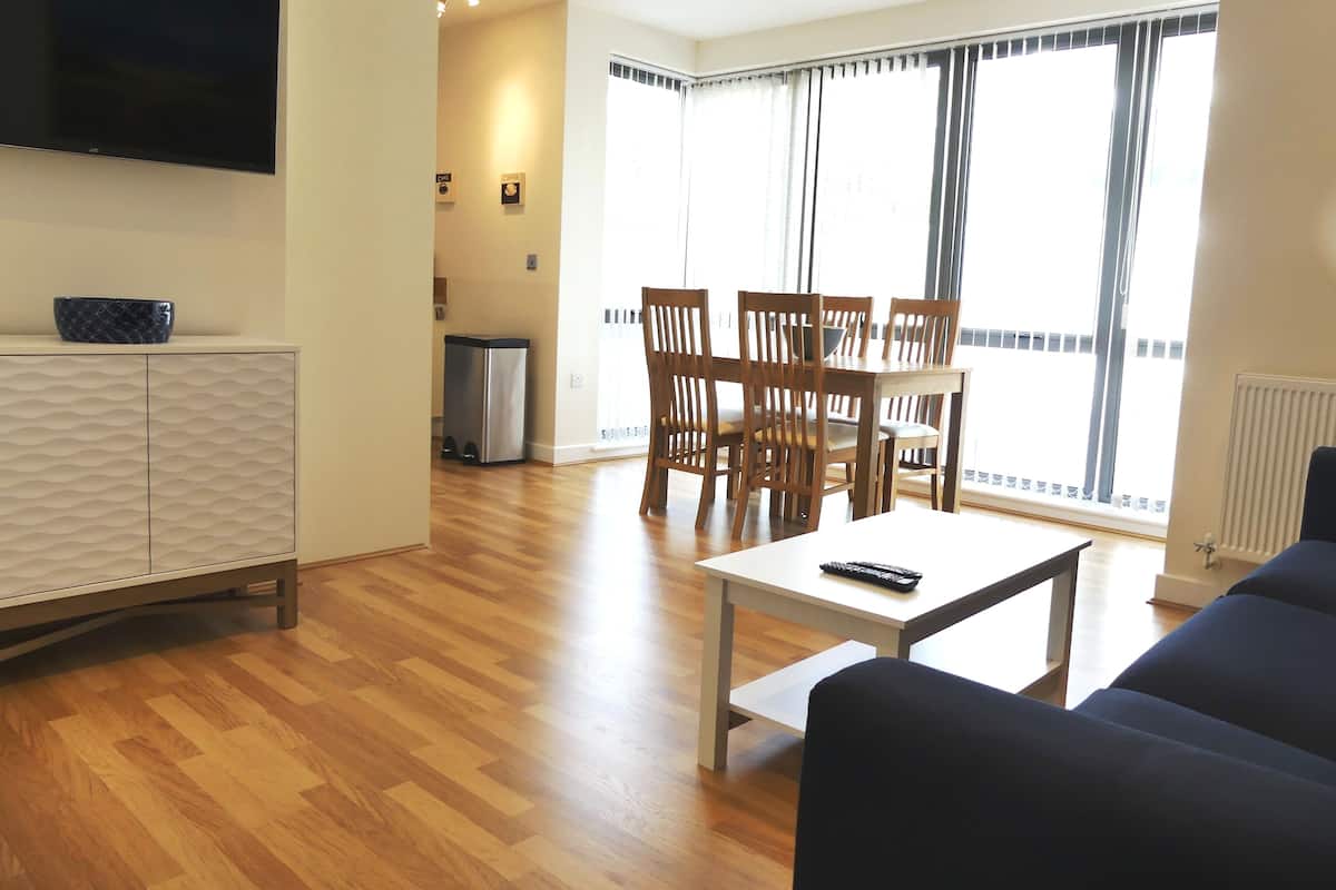 Una sala de estar con una televisión de pantalla plana, un comedor con sillas de madera, un sofá y una mesa.
