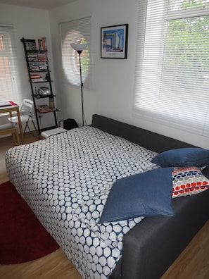 Un dormitorio con una colcha estampada, un escritorio con silla, una estantería y un cuadro en la pared.