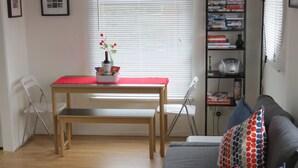 A living room with a sofa, a dining table with a red tablecloth, a bookshelf, and a window with blinds. - City Centre Belfast (Belfast)
