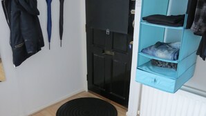 A room with a black door, a coat rack with a jacket, a blue shelf with folded clothes, and two black rugs on the floor. - City Centre Belfast (Belfast)