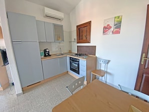 A compact kitchen with grey cabinets, a built-in oven, a coffee maker, and a small dining table with two chairs.