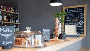 Eine Bäckereitheke mit einer Glasvitrine voller Muffins, einem Schild für Muffins, einem Schild für Saucisson und einer Kreidetafel mit der Speisekarte.