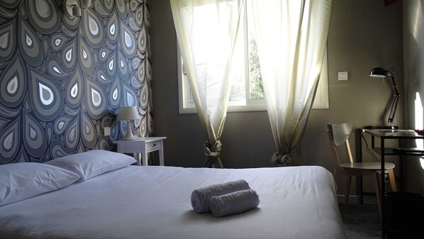 A neatly made bed with a rolled towel, a bedside table with a lamp, a chair, and curtains. - Hôtel Restaurant Logis Côté Lac (Savenay)