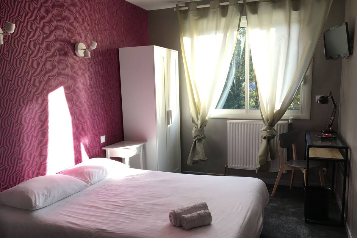 A bedroom with a bed, a desk, a chair, a wardrobe, and a window with curtains.