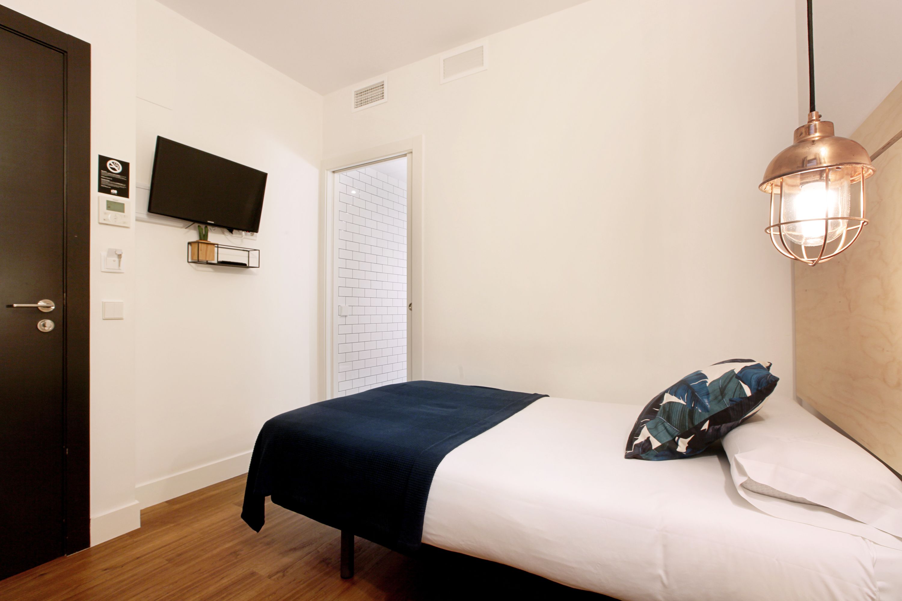 A bedroom with a bed, a television mounted on the wall, a door, and a ceiling light fixture.