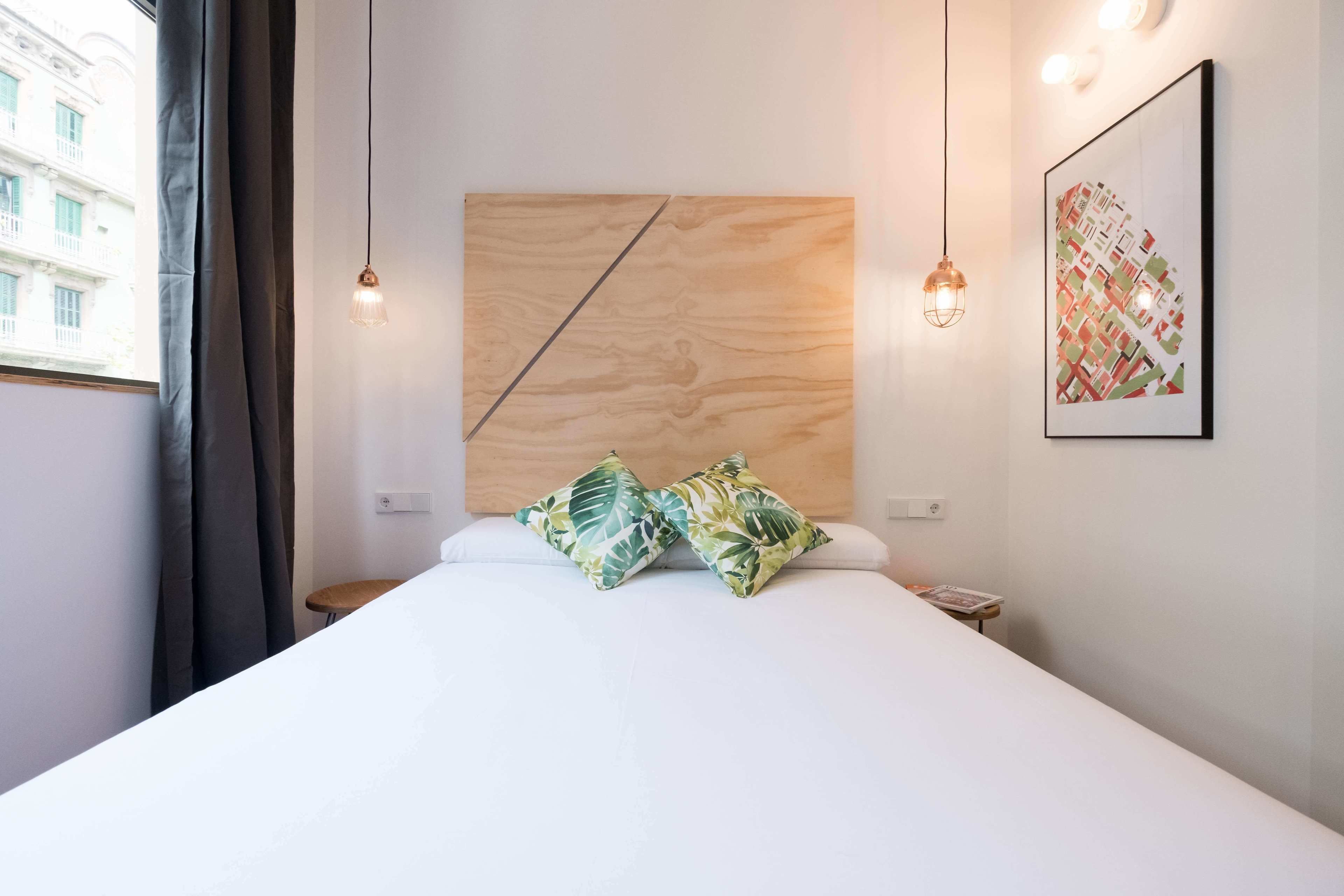 Een moderne hotelkamer met een groot bed, twee decoratieve kussens, een houten hoofdbord, een lijstwerk en een klein nachtkastje.