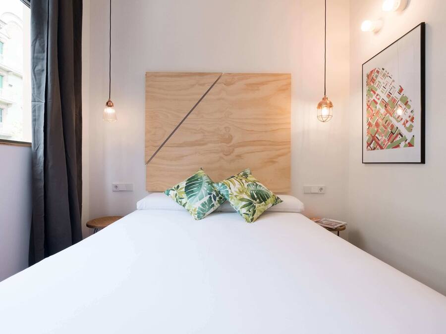 Een moderne hotelkamer met een groot bed, twee decoratieve kussens, een houten hoofdbord, een lijstwerk en een klein nachtkastje.