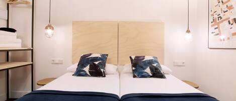 Un letto matrimoniale con testiera in legno, due cuscini, una coperta blu, un lampadario a sospensione e un quadro appeso al muro.