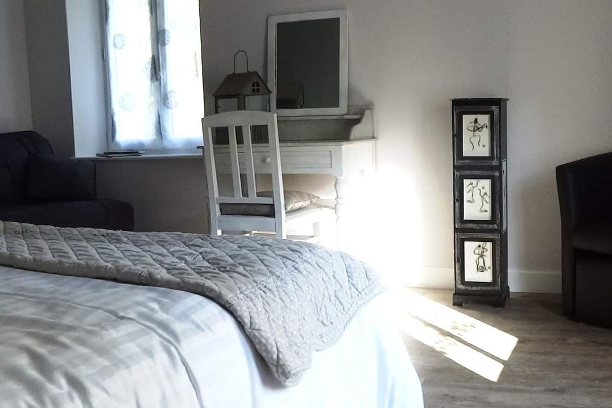A bedroom with a bed, a chair, a wardrobe, and a window with curtains.