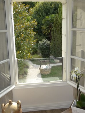 A window with a view of a garden, a stone fountain, and a potted orchid. - Le Jardin de Canaan (Saint-Julien-de-Chedon)