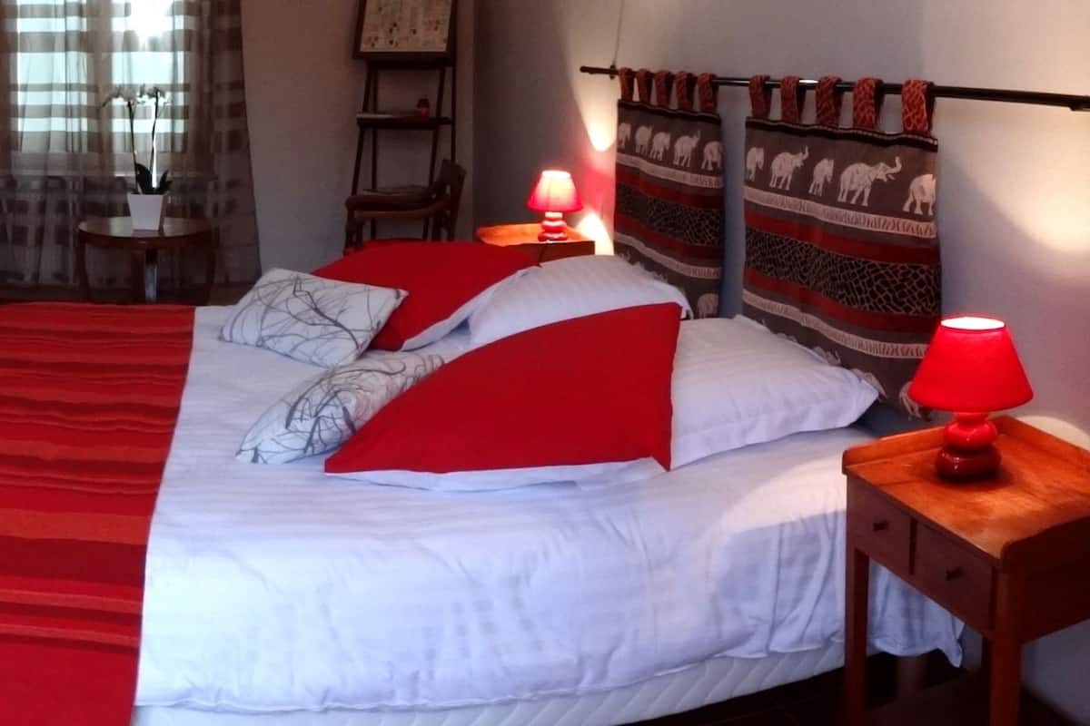 A room with a bed, a red chair, a wooden cabinet, and a small table with a lamp.