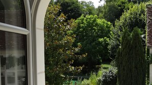 A view through an arched window of a garden with a gravel path, a stone bench, and various shrubs and trees. - Le Jardin de Canaan (Saint-Julien-de-Chedon)
