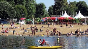 A crowded beach with people sunbathing and swimming. There are several umbrellas and a white tent in the background. - Le Jardin de Canaan (Saint-Julien-de-Chedon)