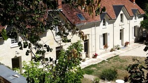 A traditional building with a tiled roof, multiple windows, and a courtyard with potted plants and outdoor seating. - Le Jardin de Canaan (Saint-Julien-de-Chedon)