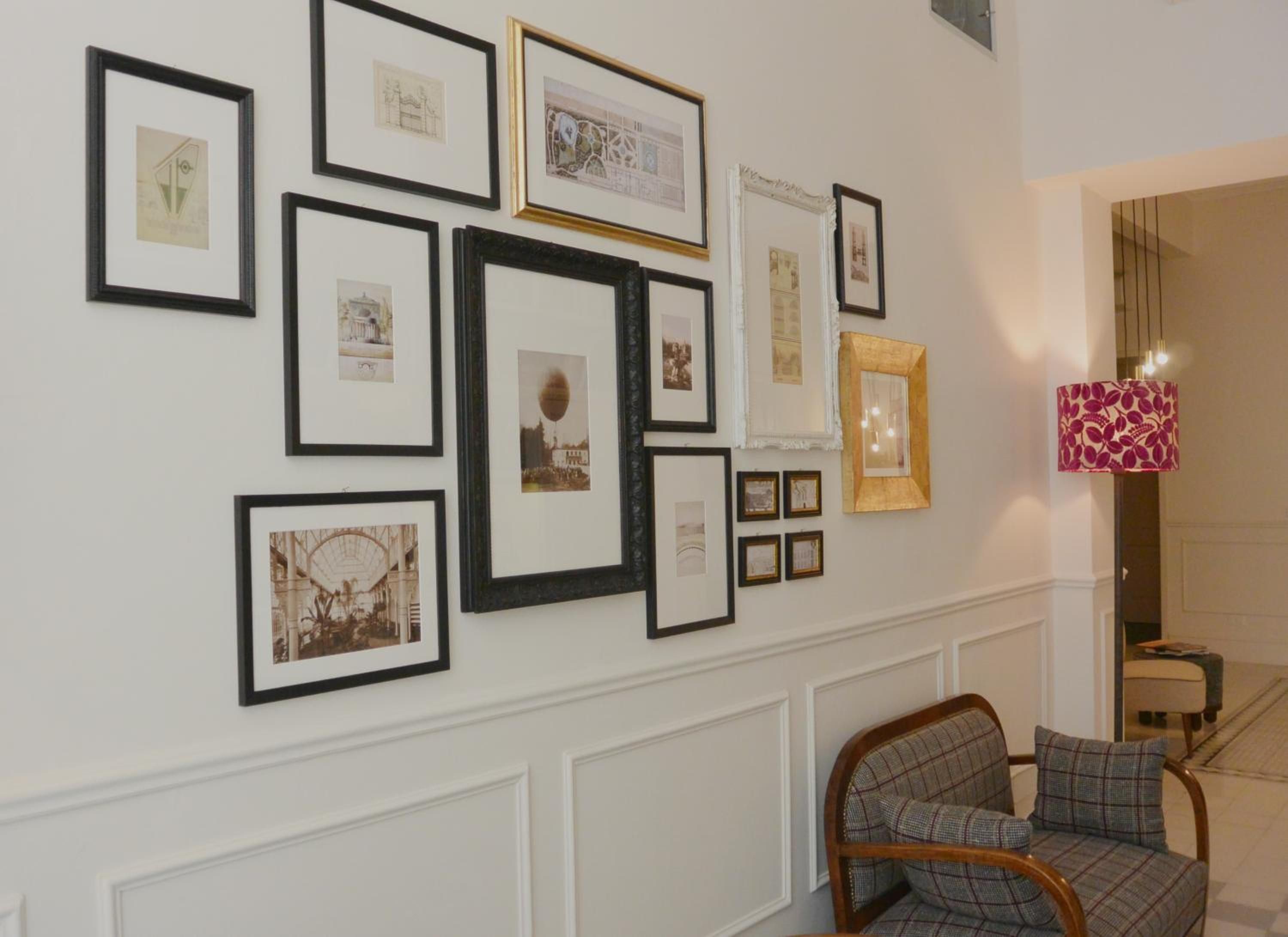 A wall with multiple framed pictures, a patterned lamp, and a plaid chair.