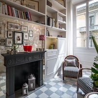 Quarto com lareira, estantes de livros, quadros emoldurados e janela com vista para edifícios.